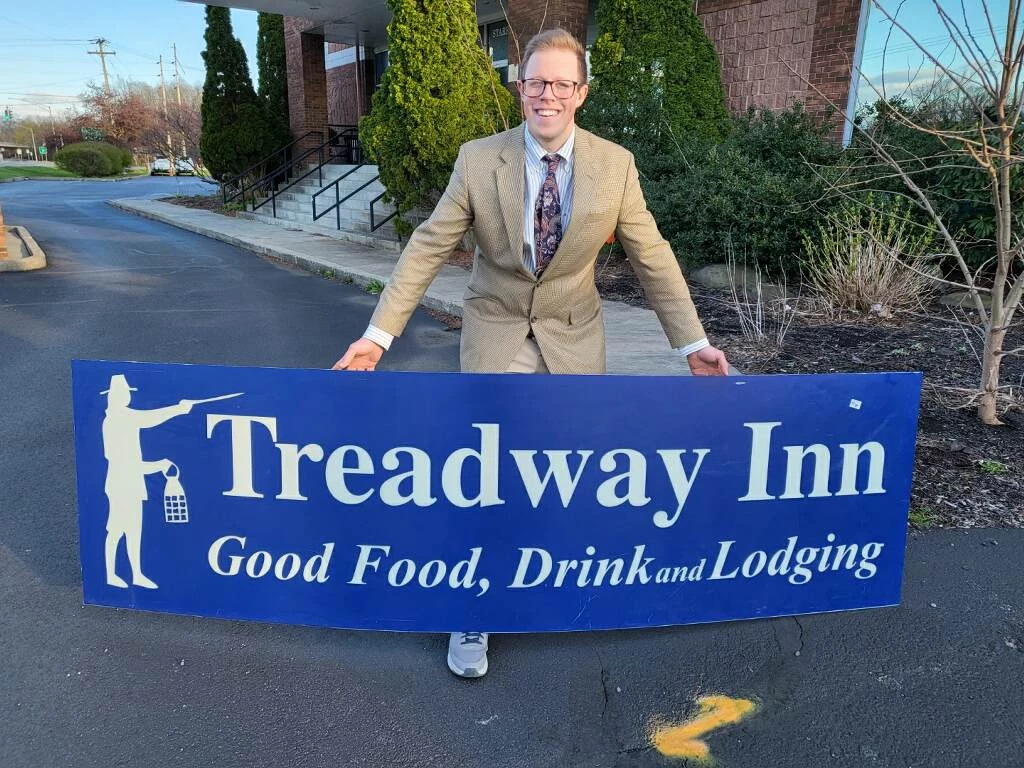 Local Auctioneer Luke Kaczynski, of Mead & Sons Auctioneers of Owego, helped conduct the Owego Treadway liquidation auction on Saturday, April 20th. Here he poses with the original outdoor sign before the historic Treadway is demolished. 